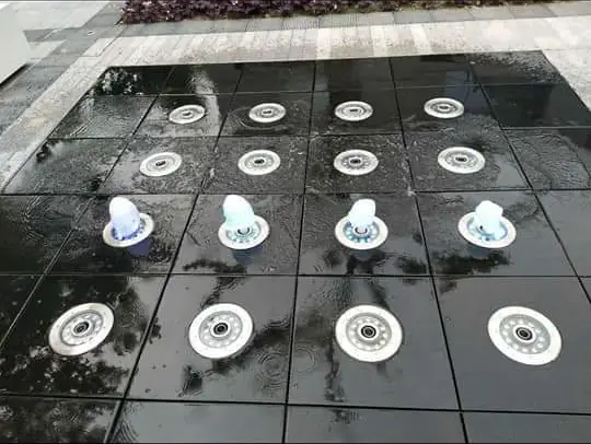 Deck fountain with nozzles flush in the paving
